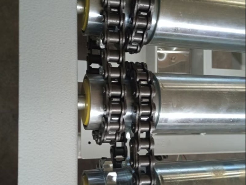 Technical close-up view of sprocket-driven conveyor rollers and drive chains